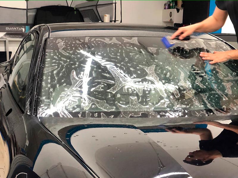 Смотреть на фото, как мастера фирмы AR-Detailing монтируют на лобовое стекло автомобиля защитную пленку.