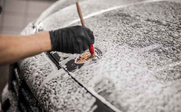 На фото технолог детейлинг-центра AR-Detailing кистью чистит эмблему на капоте автомобиля Porsche.
