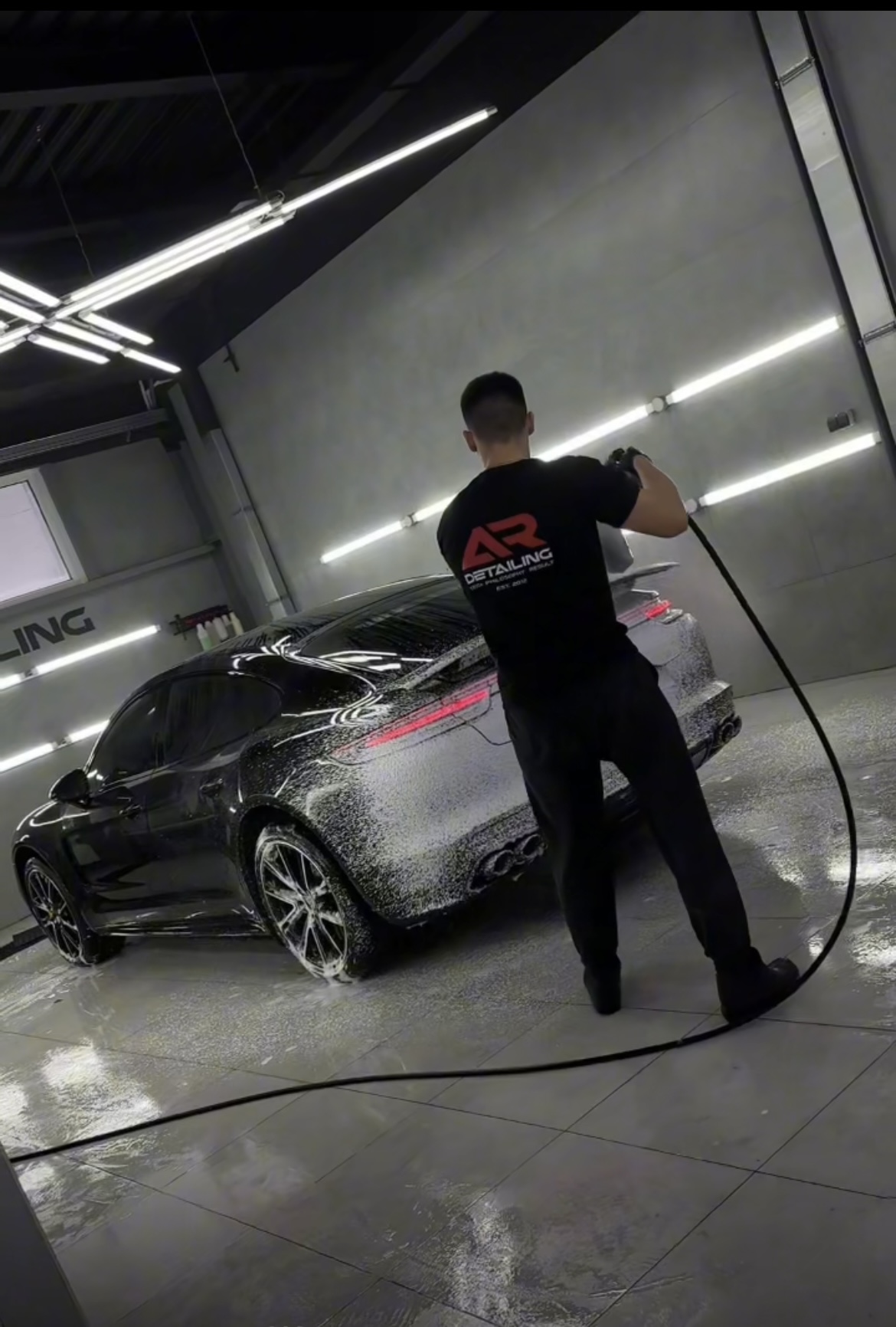 На фото технолог детейлинг-центра AR-Detailing кистью чистит эмблему на капоте автомобиля Porsche.