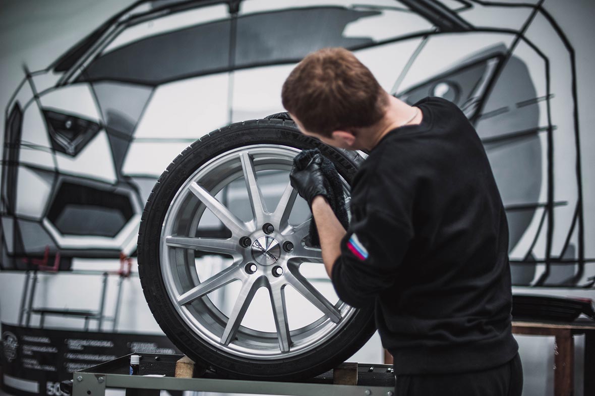 На фото мастер детейлинг-центра обрабатывает керамикой отполированный колесный диск автомобиля. 